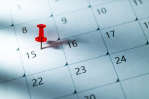 Red thumbtack on the 15th of calendar with light rays and shadow