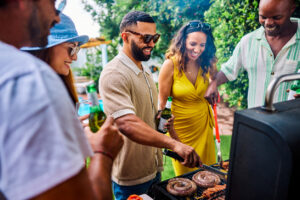 Diverse group of friends and family grilling sausages, corn, and chicken skewers at a barbecue party. Outdoor social gathering. Summer food and cooking concept.