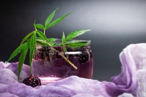Water with fresh, ripe blackberries and cannabis. Refreshing, relaxing non-alcoholic cocktail on hot summer days. In a glass cup on decorative dark background, with copy space
