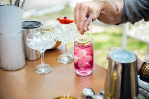 Making of a pink cocktail with ice, lime and spices outdoors. The bartender makes a refreshing summer alcoholic or non-alcoholic cocktail on outdoor party. Outdoor cocktail party.